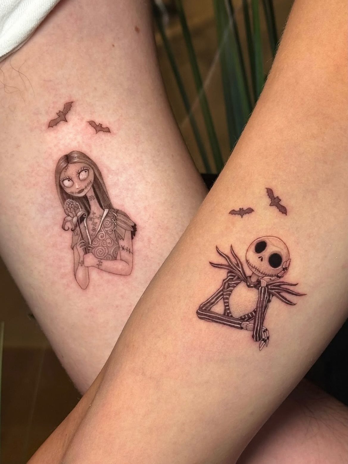 Black and white tattoos of Jack Skellington and Sally on two different arms.