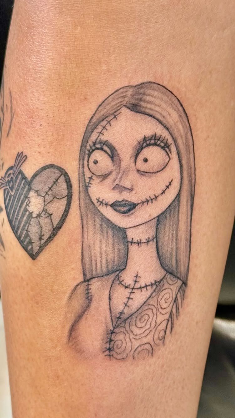 Sally tattoo with a stitched heart and arrow on a person's skin.