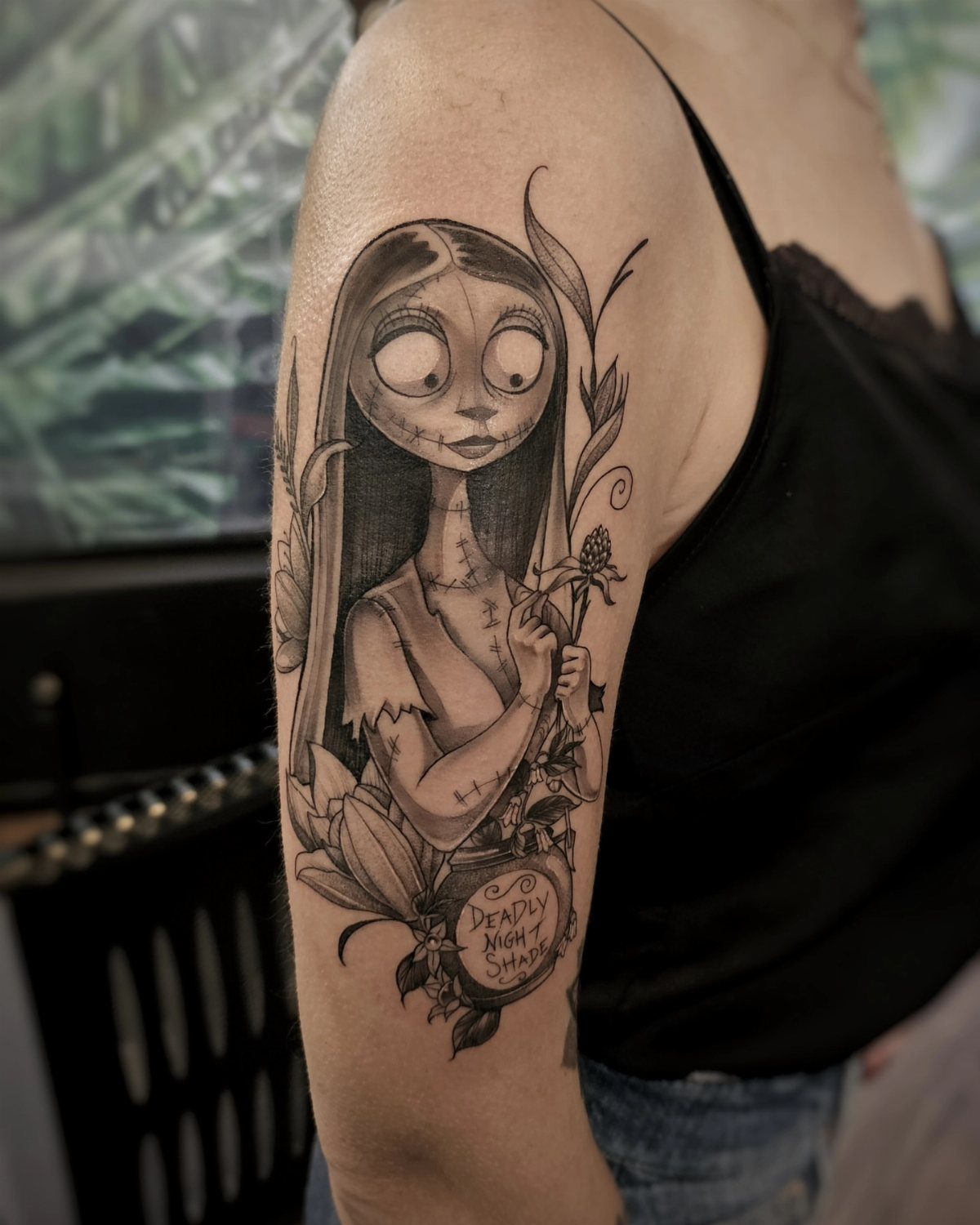 Sally tattoo on an upper arm with floral details and a small plaque.