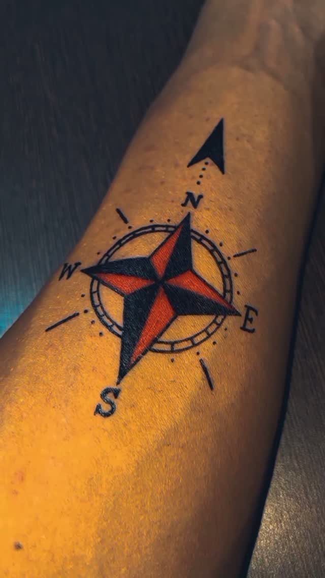 Compass rose tattoo with red and black star on a person's forearm.