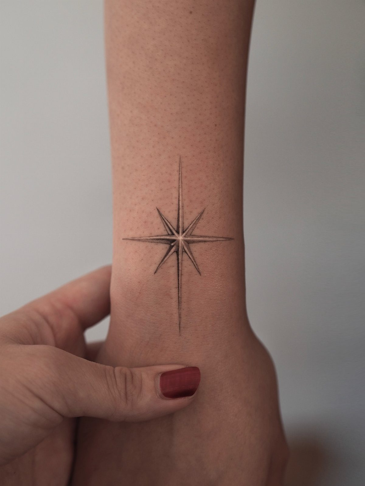 North star tattoo on a wrist with thin black lines and sharp points.