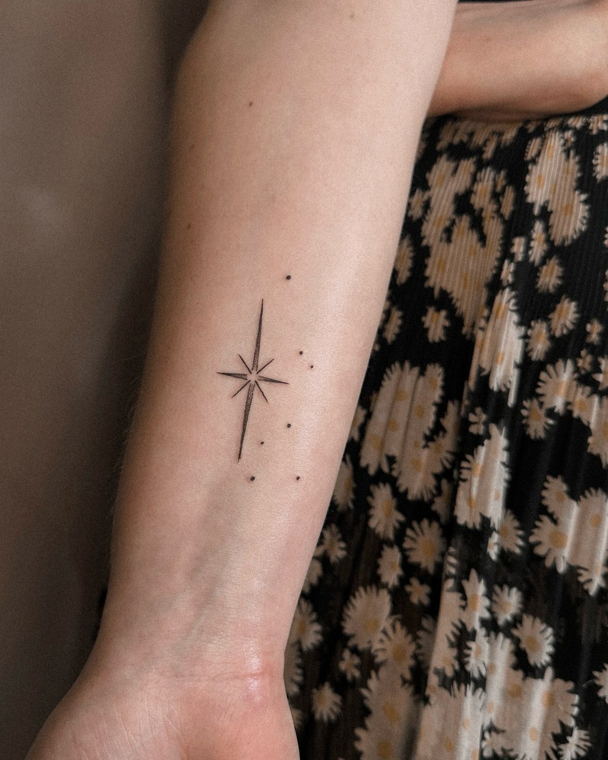 Small black north star tattoo with fine lines on a person's inner forearm.