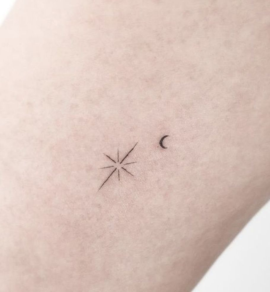 Minimalist north star and crescent moon tattoo in black ink on pale skin.