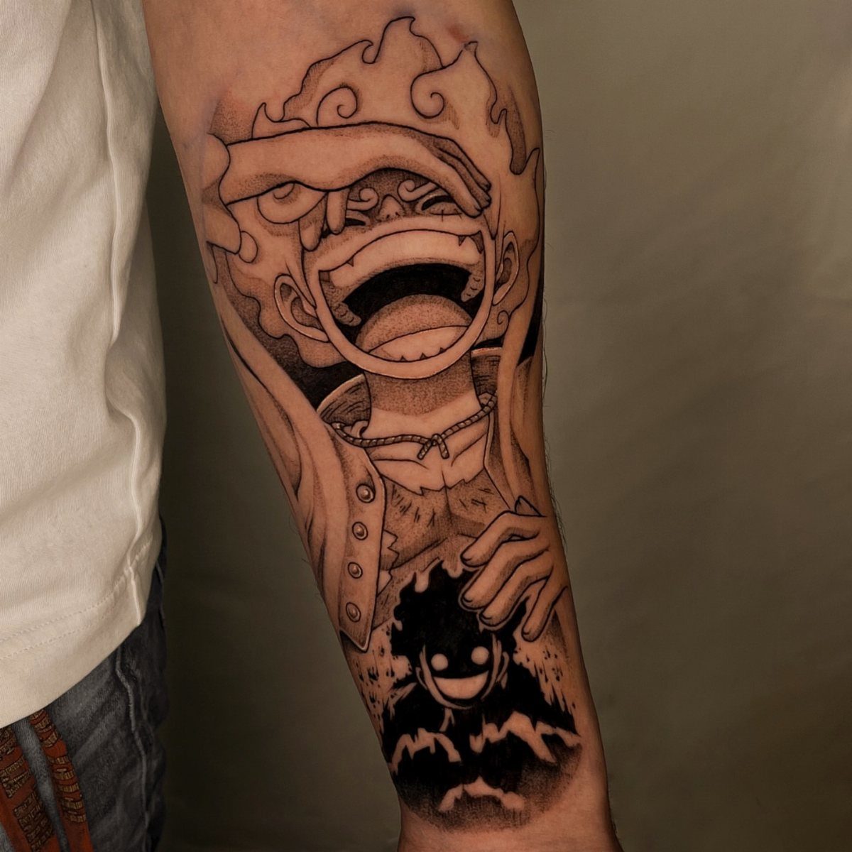 Luffy Gear 5 tattoo on a forearm featuring his laughing face and cloud hair.