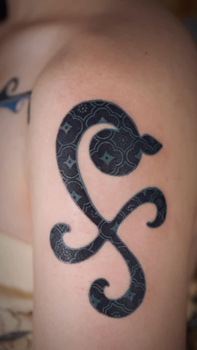 Black ink pinwheel and orange tattoo on a person's shoulder with floral patterns.