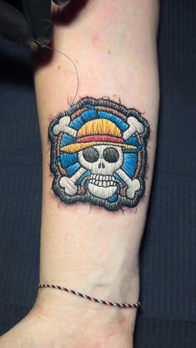 Straw Hat Pirates skull tattoo designed as a realistic embroidered fabric patch on skin.