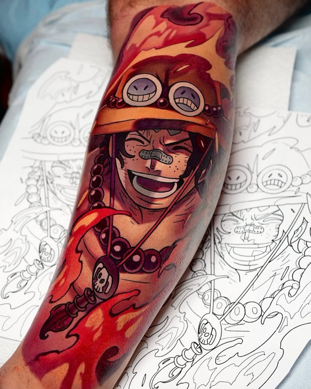 Portgas D. Ace tattoo on an arm with red flames and orange hat.