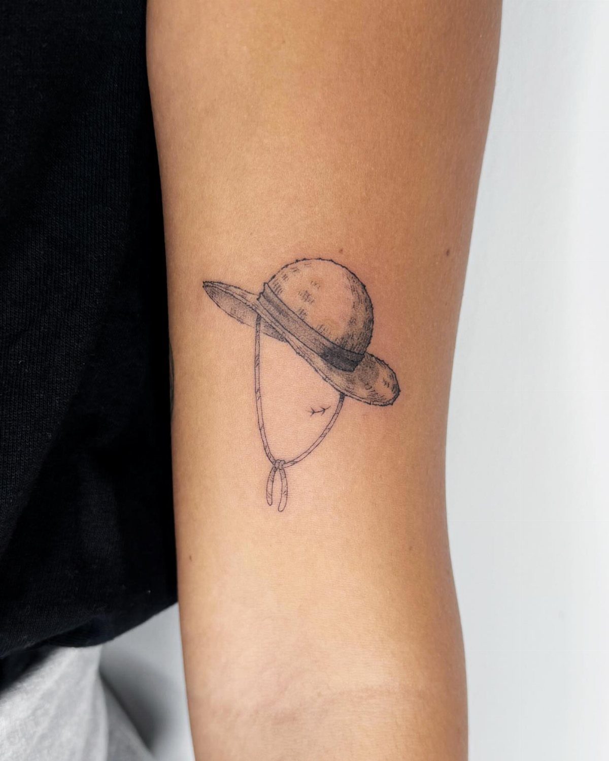 Straw hat tattoo with a chin strap on a person's inner forearm.