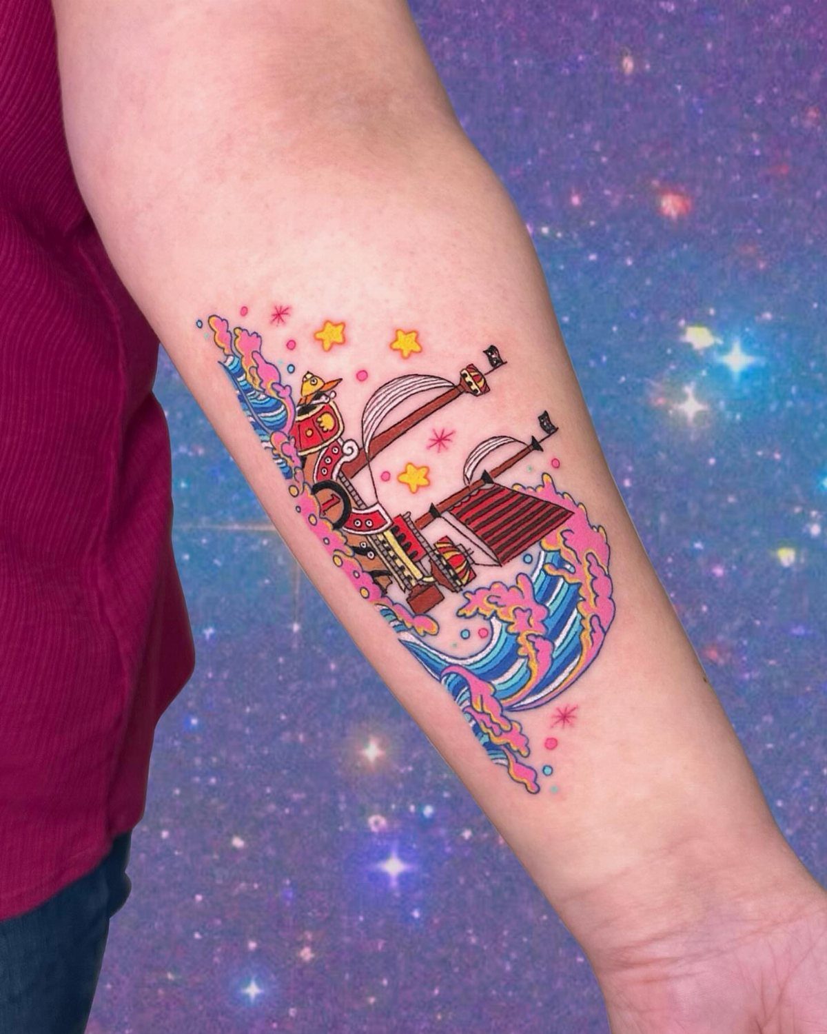 Thousand Sunny ship tattoo on a forearm with blue waves and yellow stars.