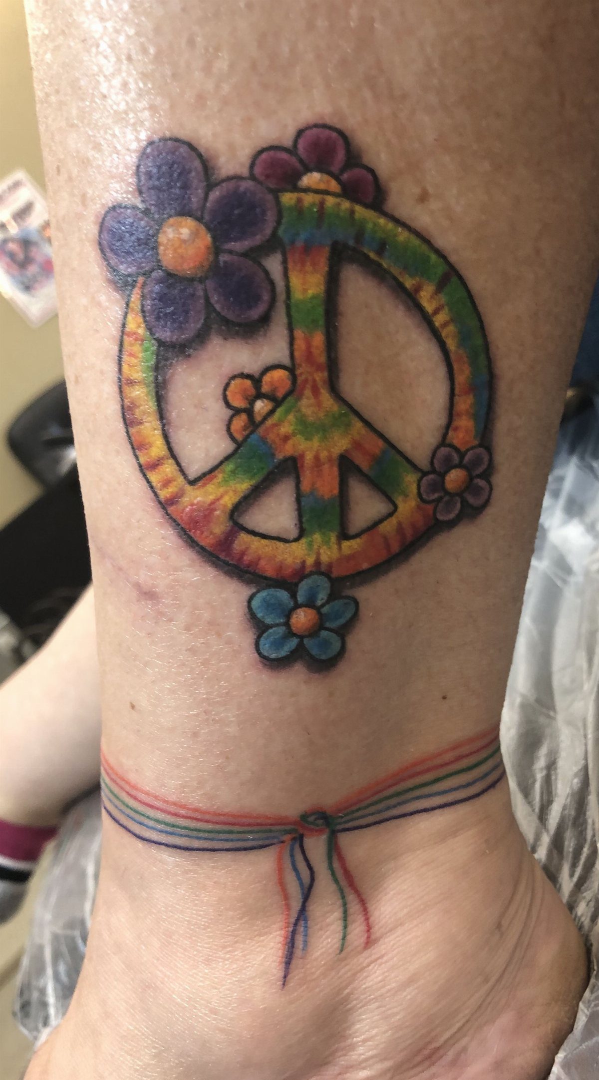 Rainbow peace sign tattoo with colorful flowers on a person's ankle