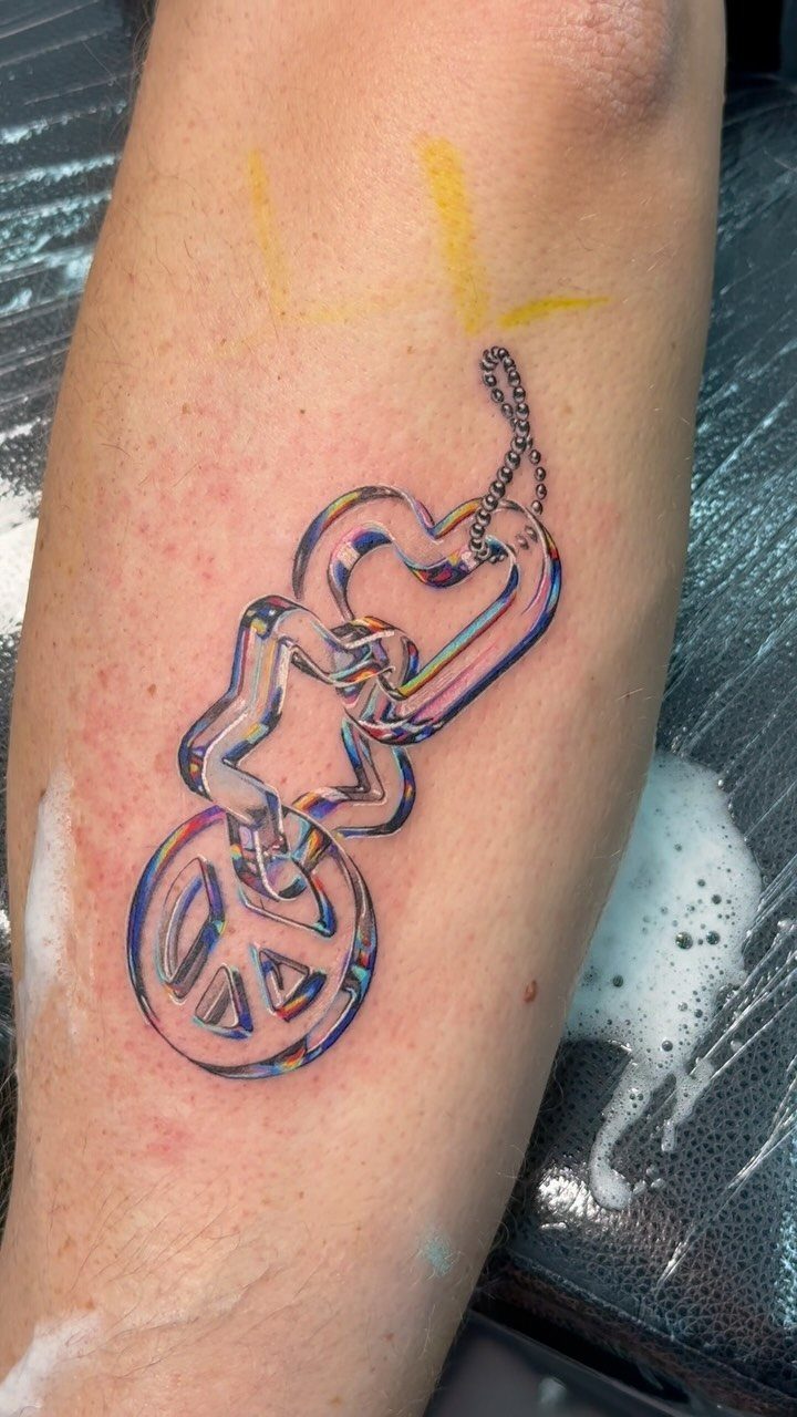 Colorful tattoo of a peace symbol hanging from a chain of iridescent hearts.