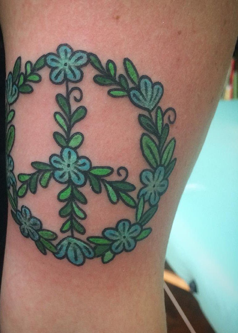 Peace sign tattoo composed of blue flowers and green leaves on skin