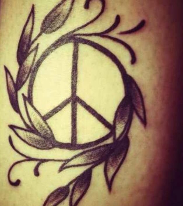 Peace symbol tattoo encircled by a leafy olive branch on human skin.