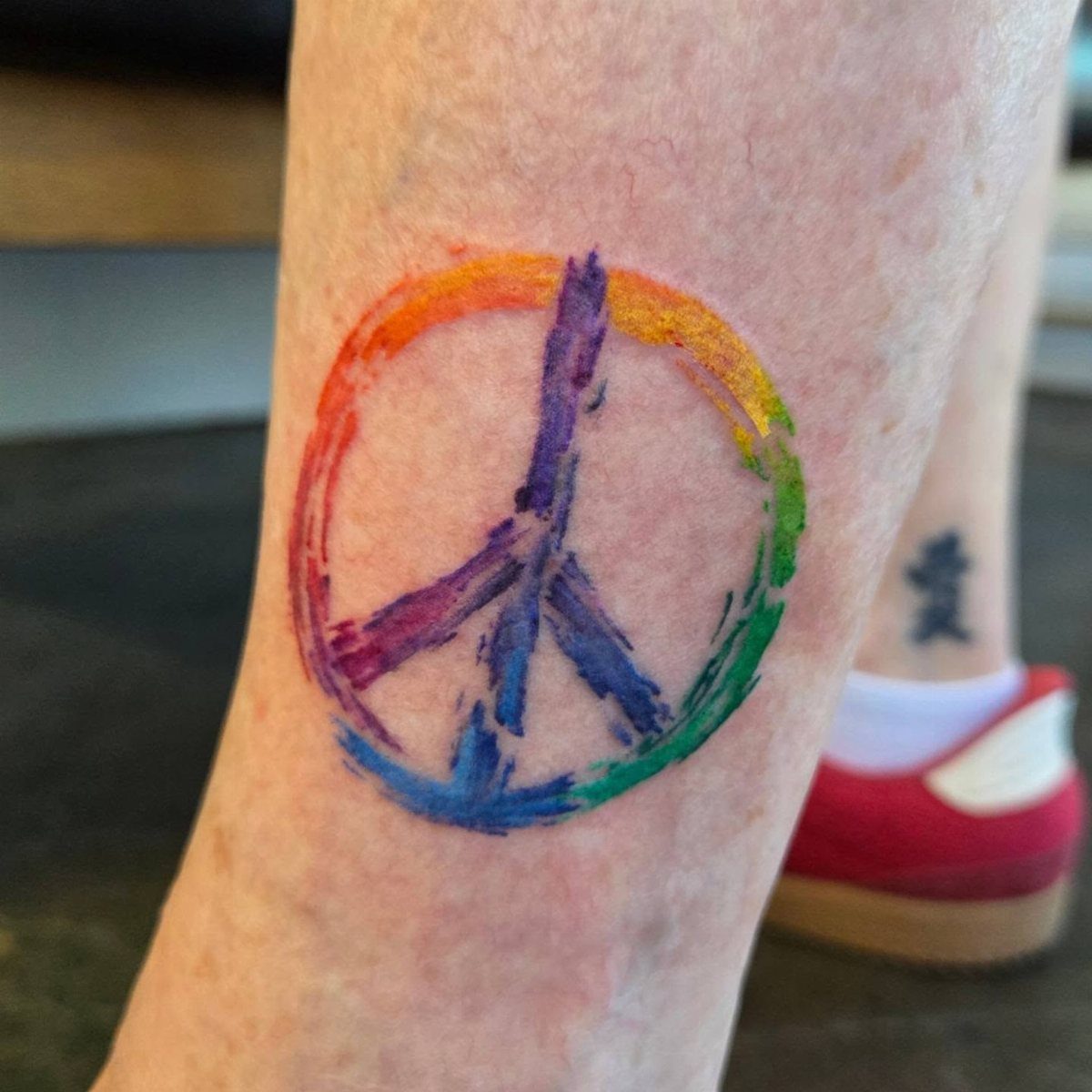 Rainbow watercolor peace sign tattoo on a person's lower leg.