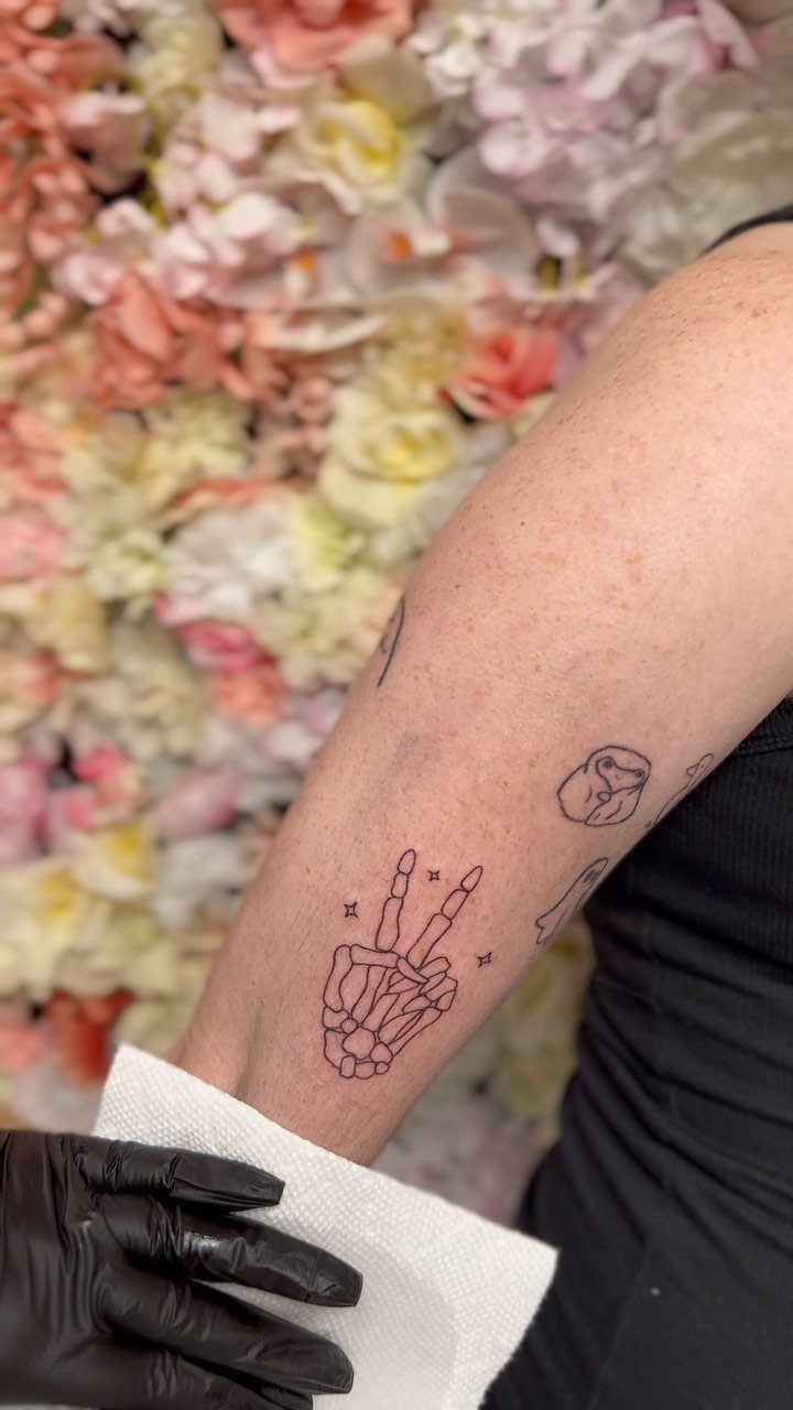 Skeleton hand making a peace sign tattoo on a person's forearm