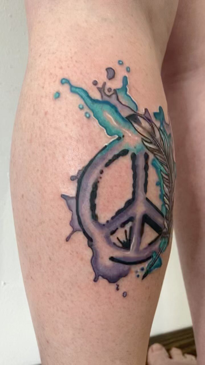 Peace sign tattoo with purple and teal watercolor splashes and a feather on skin