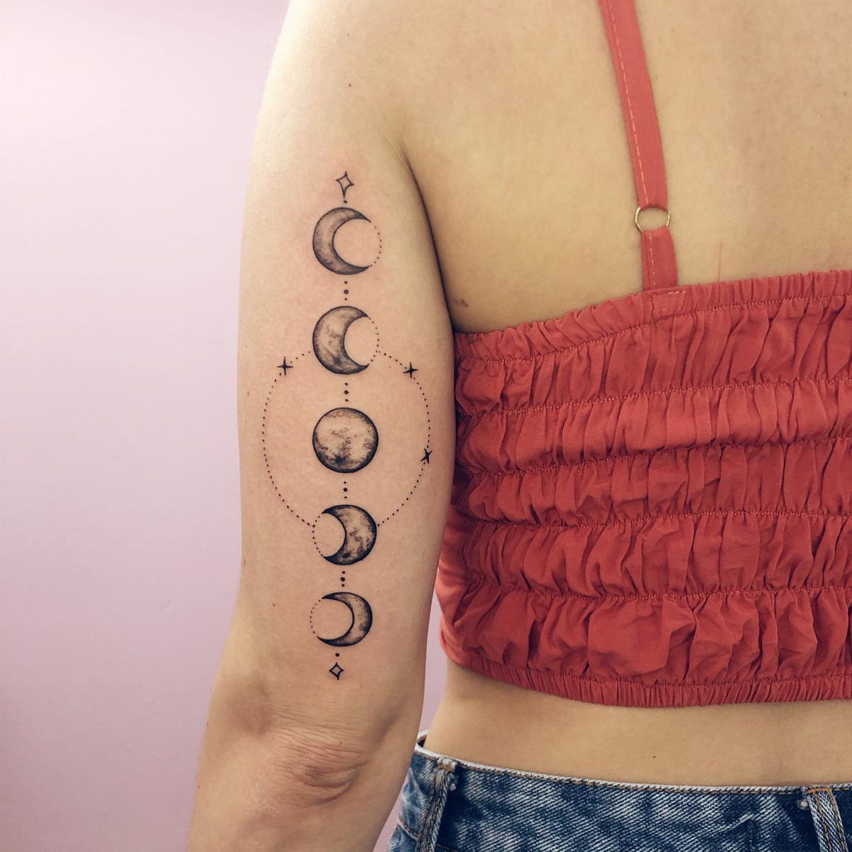 Moon phases tattoo with small stars on a person's upper arm.
