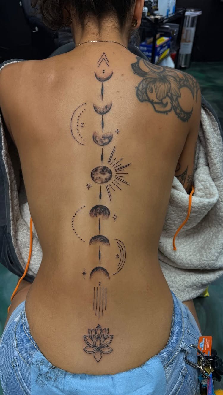 Moon phases tattoo running vertically down a person's spine with a lotus flower.