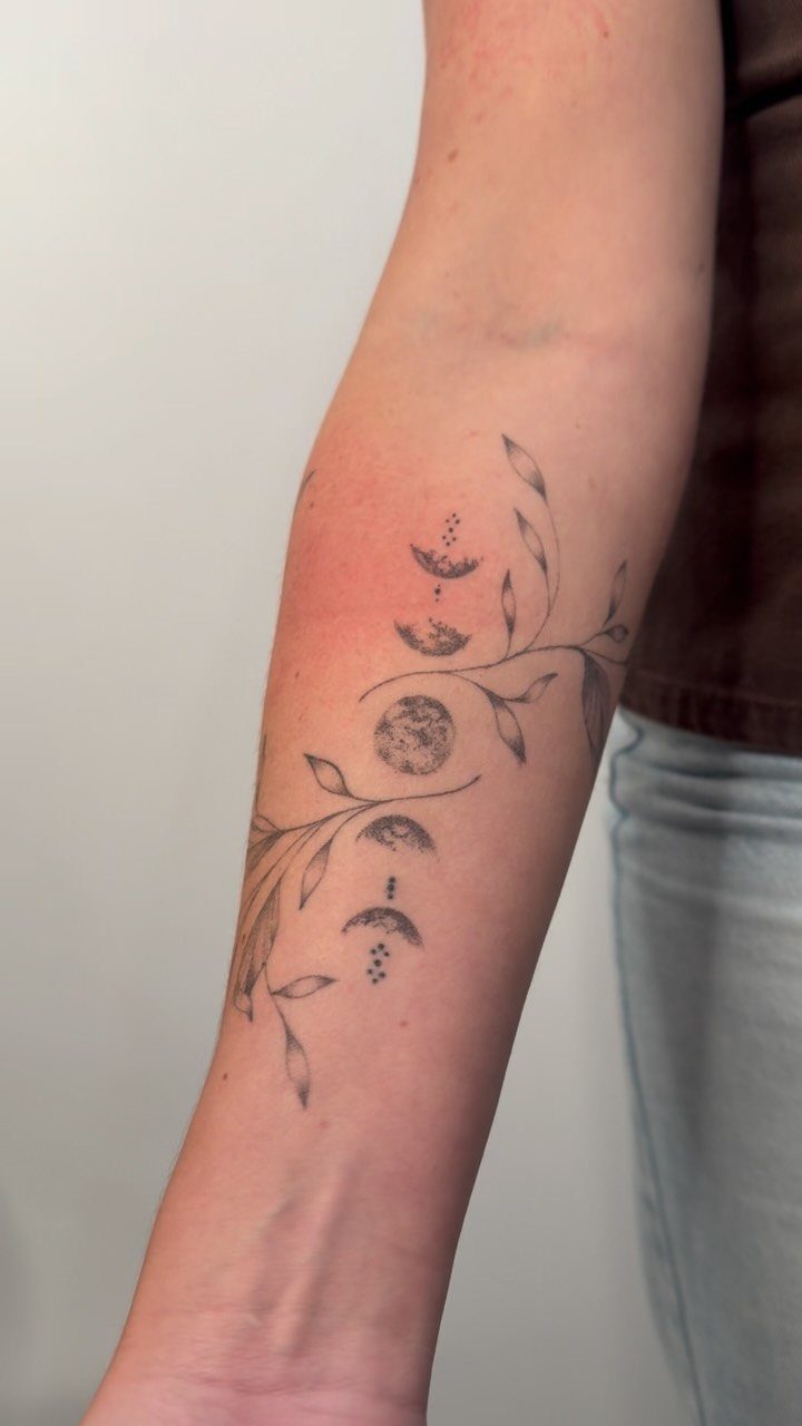 Phases of the moon tattoo with botanical branches on a person's forearm