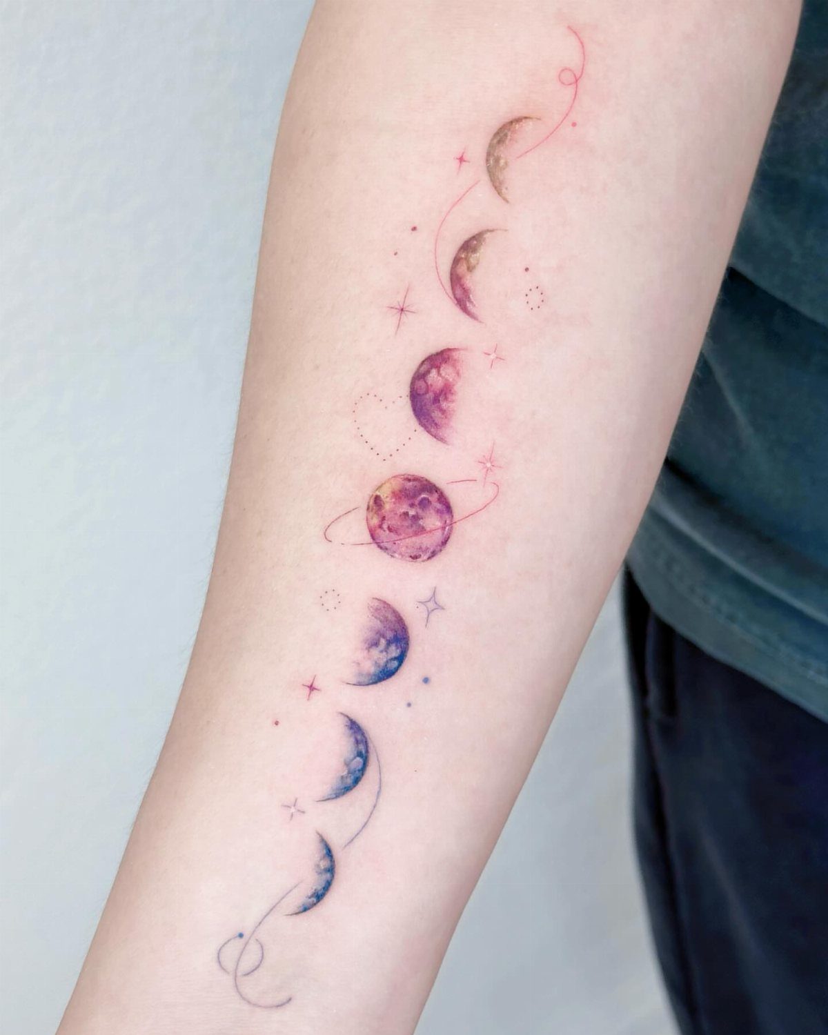 Colorful moon phases tattoo on an upper arm with purple, red, and blue ink.