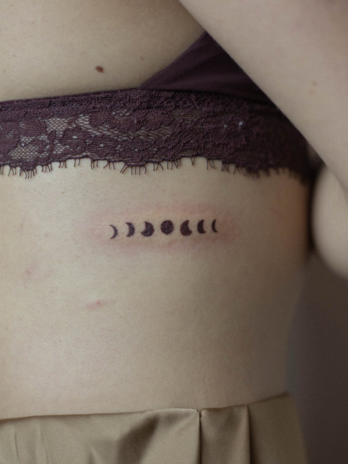 Moon phases tattoo on a person's ribcage below a purple lace bra.