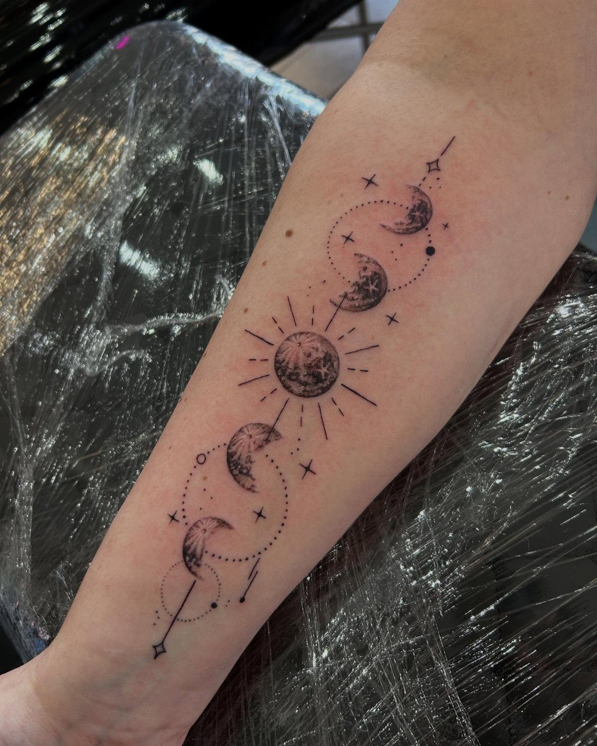 Moon phases tattoo on a forearm with sunburst rays and small stars.