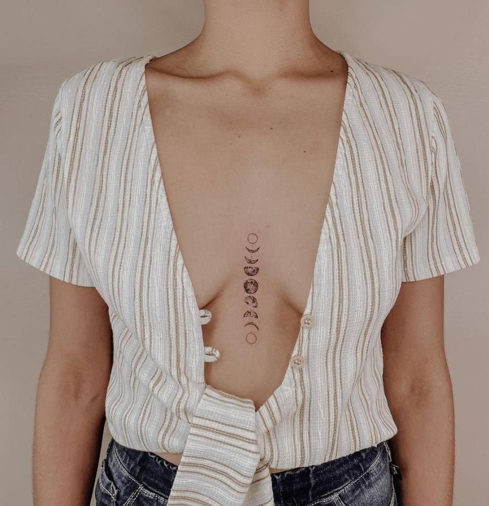 Moon phases tattoo vertically aligned on a person's sternum, wearing a white striped shirt.
