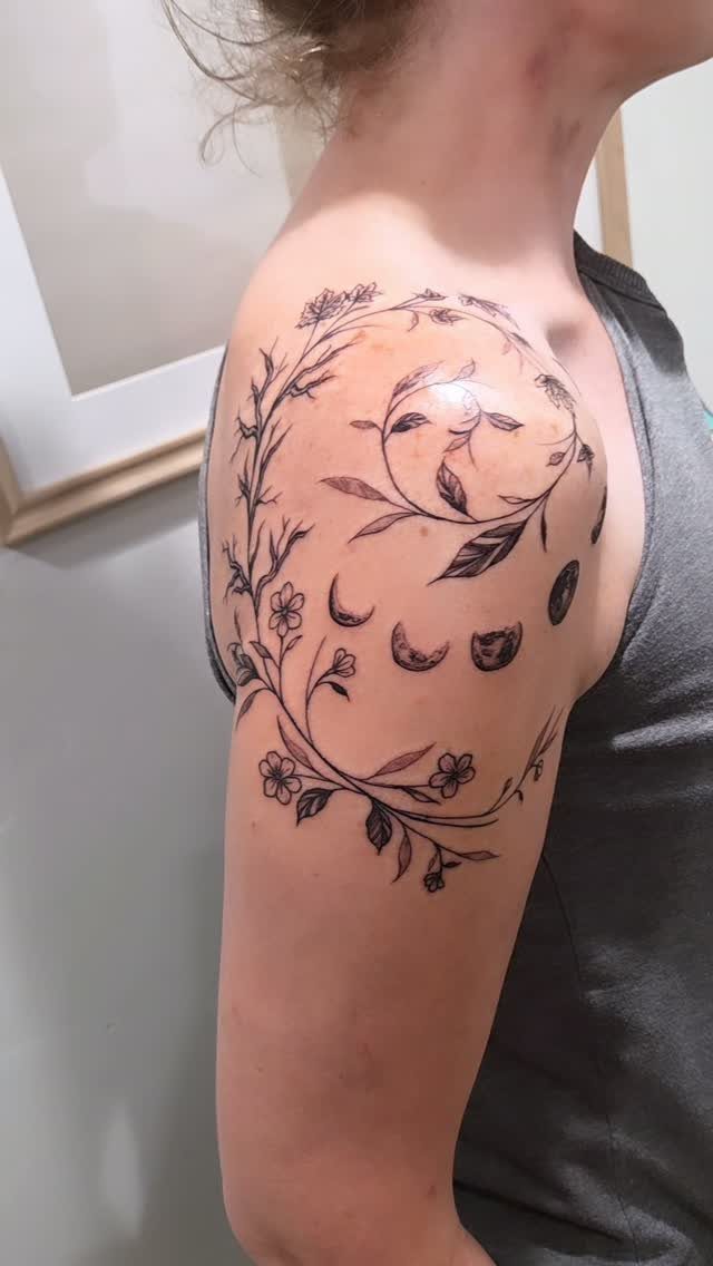 Phases of the moon tattoo surrounded by a floral wreath on a shoulder.