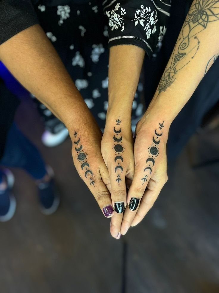 Moon phase tattoos running vertically down the center of three different hands.