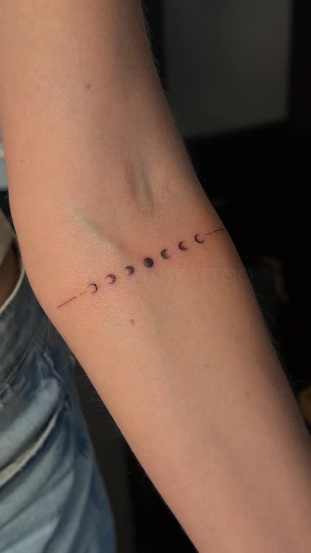 Phases of the moon tattoo in black ink on a person's inner forearm.