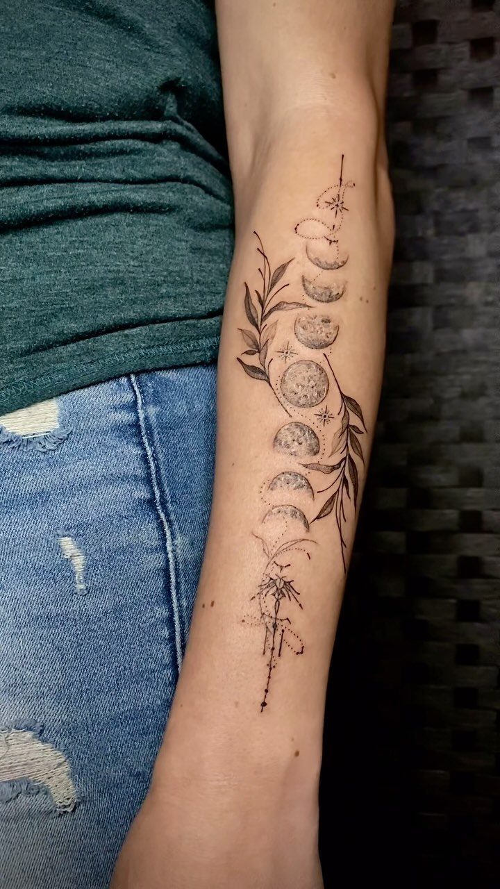 Moon phases tattoo with botanical branches and stars on a person's forearm.