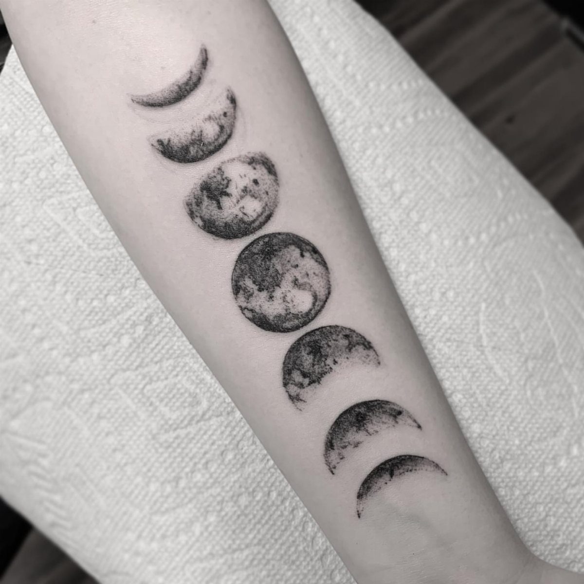 Moon phases tattoo on a forearm featuring realistic black and grey lunar cycles.