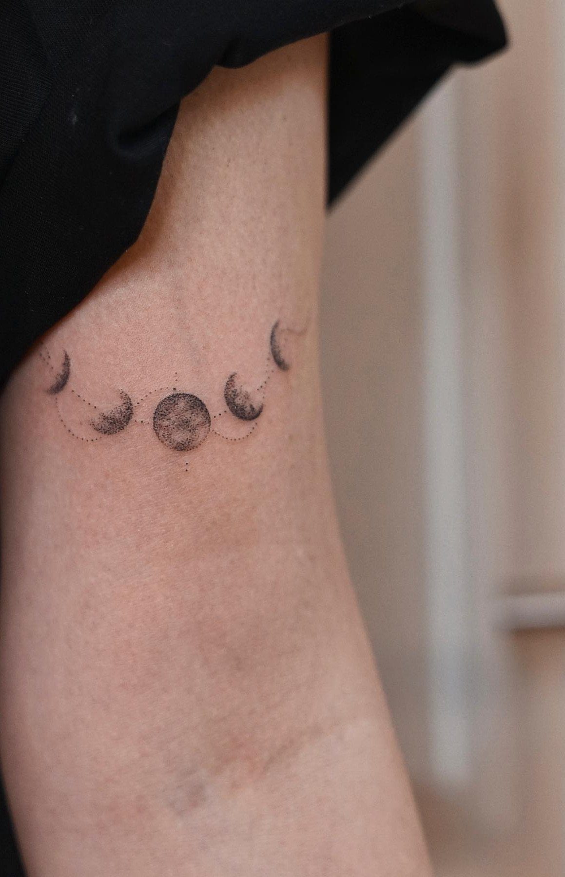 Moon phases tattoo in black ink curved across the back of an arm.
