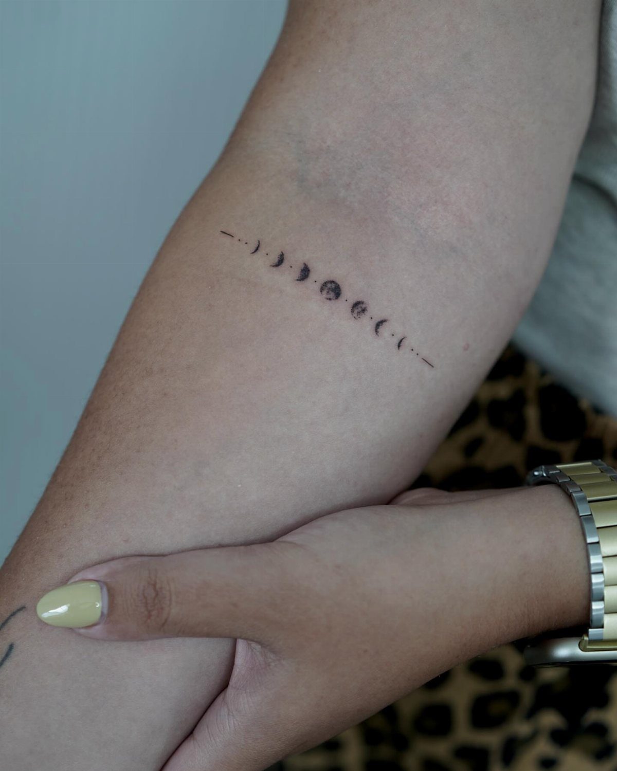 Minimalist moon phases tattoo in black ink on a person's upper arm.