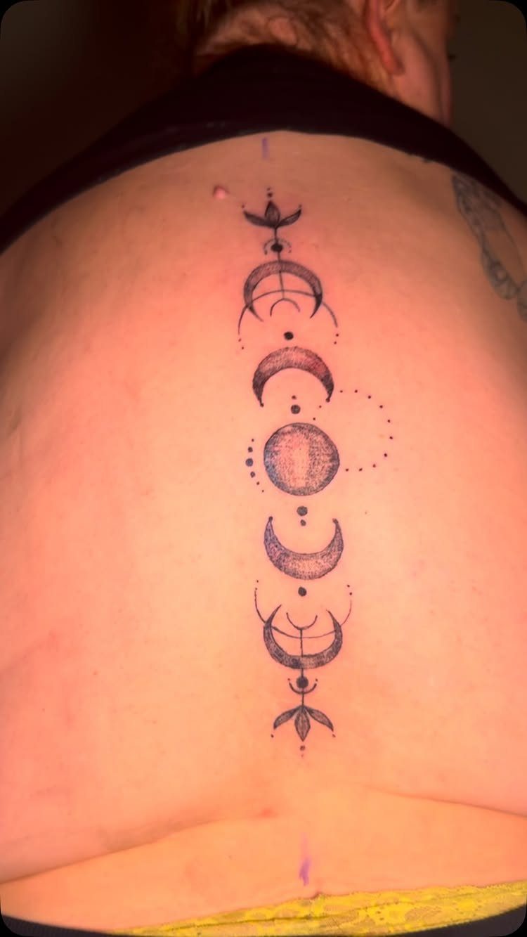 Vertical moon phases tattoo in black ink centered on a person's spine.