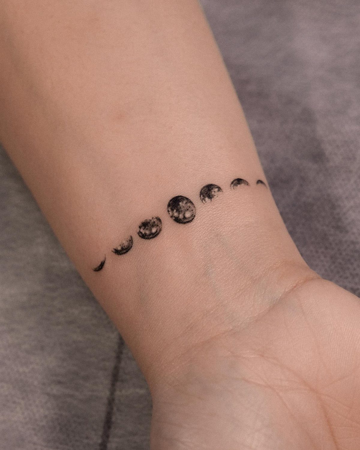 Moon phases tattoo in black ink curved around a person's wrist.
