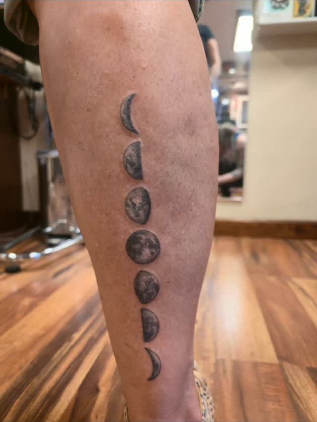 Phases of the moon tattoo in black ink on a person's lower leg.