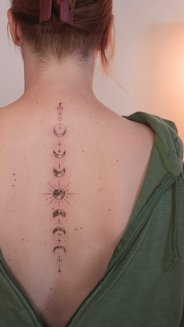Vertical moon phases tattoo with a central sunburst on a person's spine.