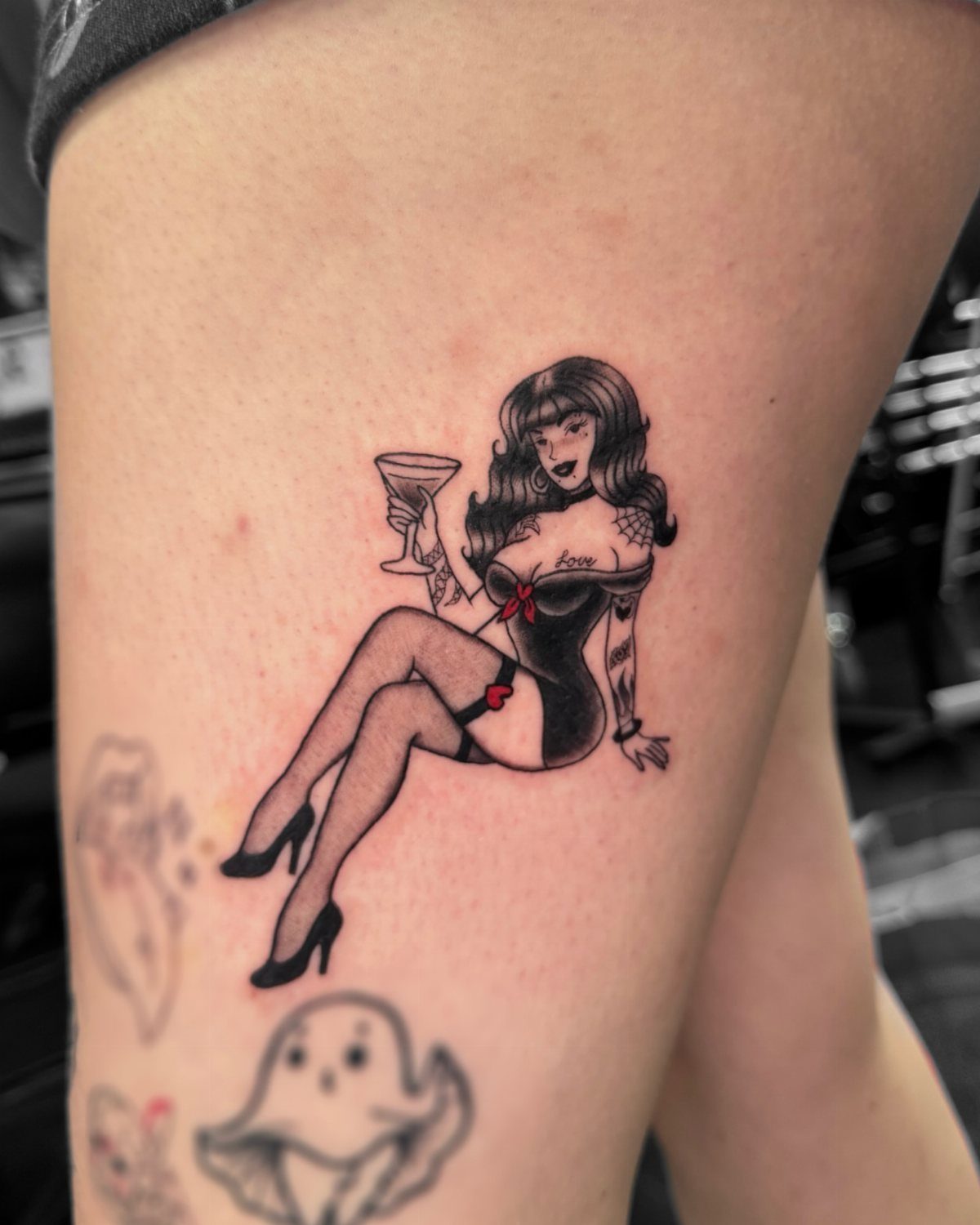 Pin-up girl tattoo on a thigh holding a cocktail glass with red accents.