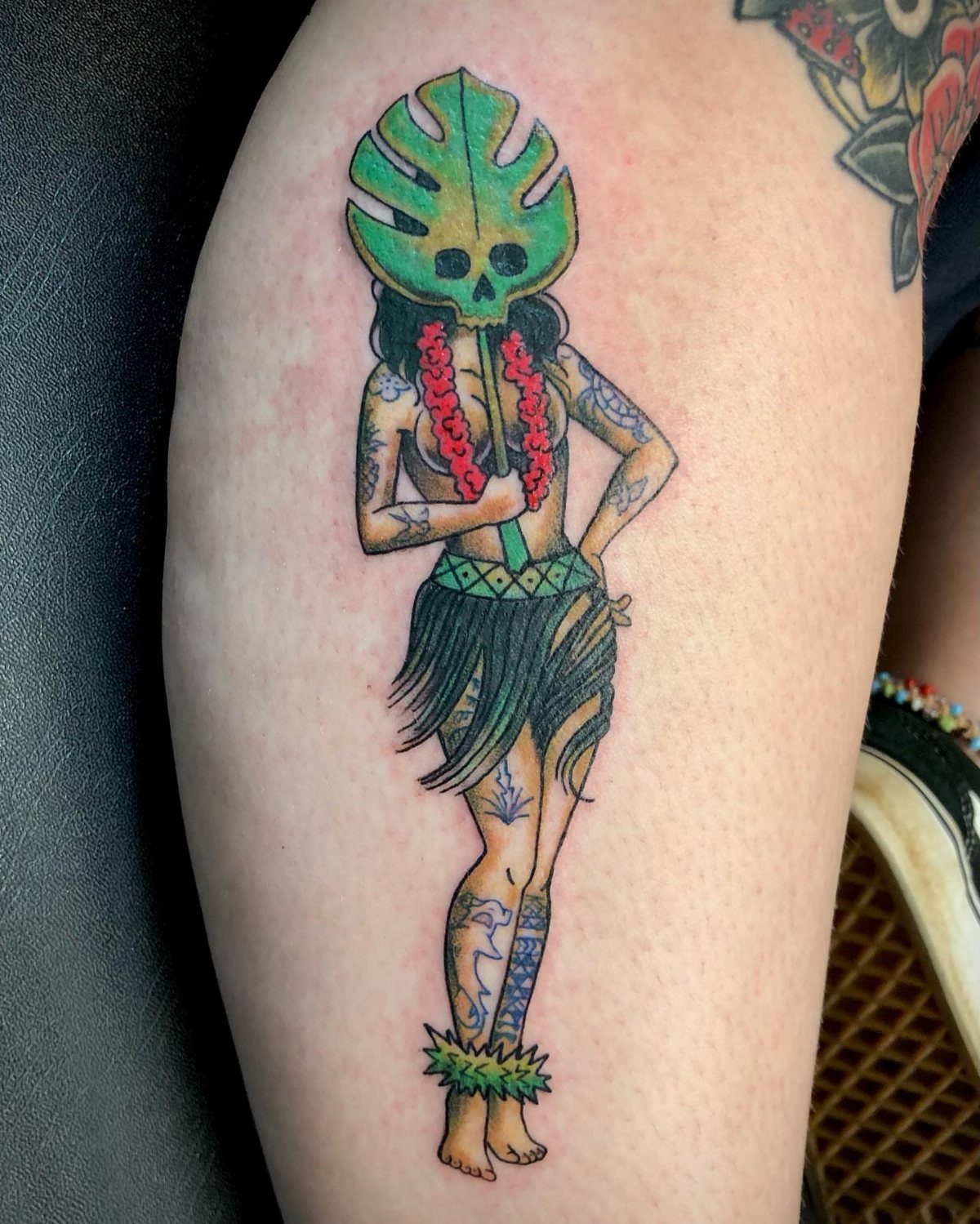 Hula girl pin-up tattoo with a leaf mask and grass skirt on a leg