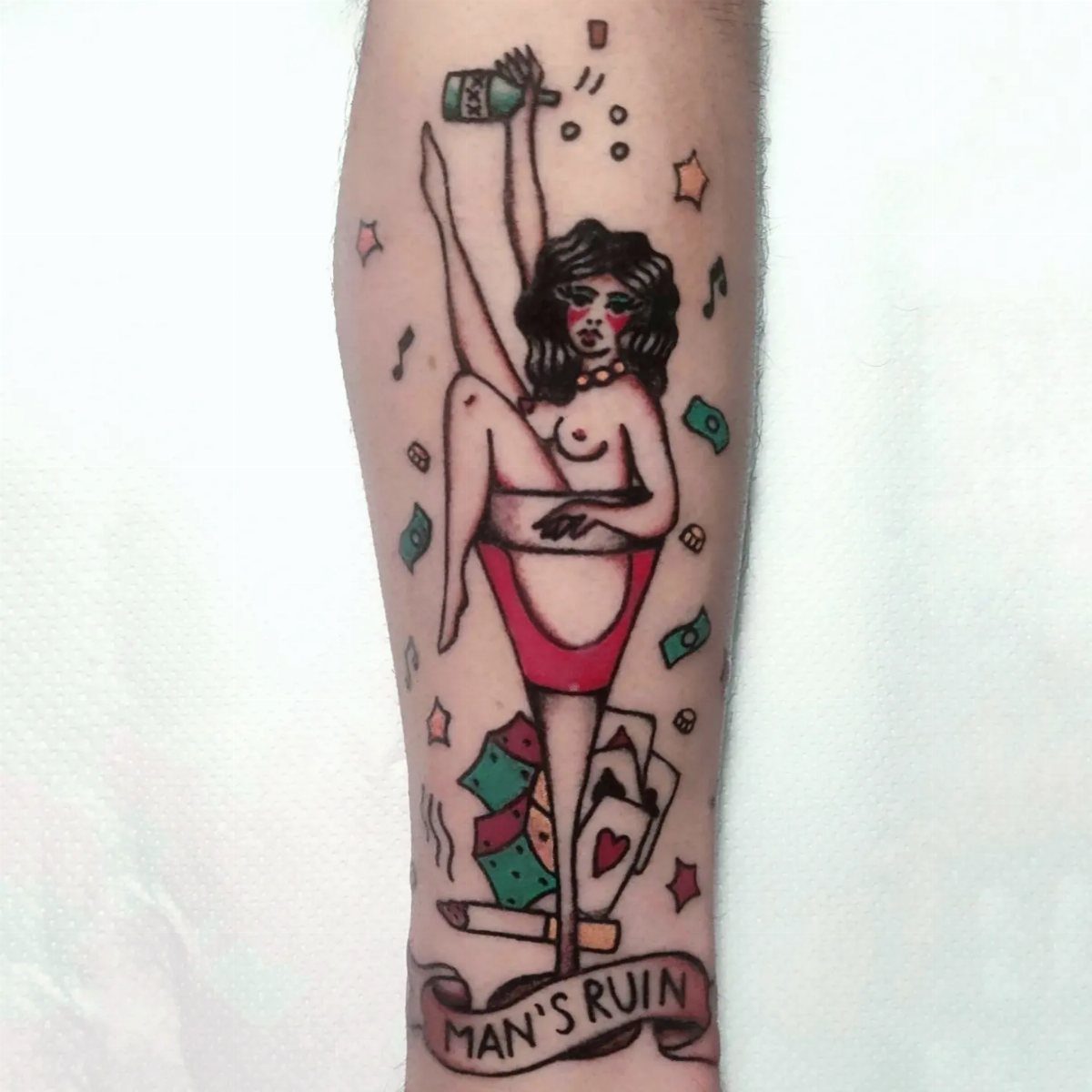 Man's Ruin tattoo on an arm featuring a pin-up woman with cards and money