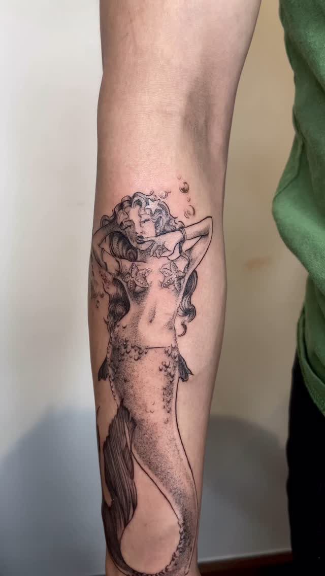 Mermaid pin-up tattoo on a forearm featuring a woman with a fish tail.