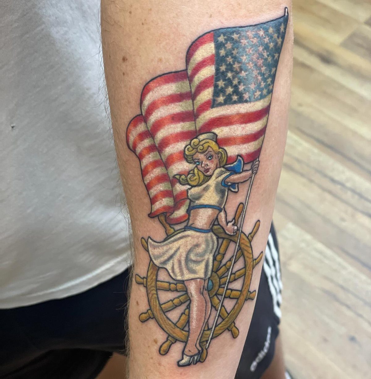 Pin up girl sailor tattoo with American flag and ship wheel on arm