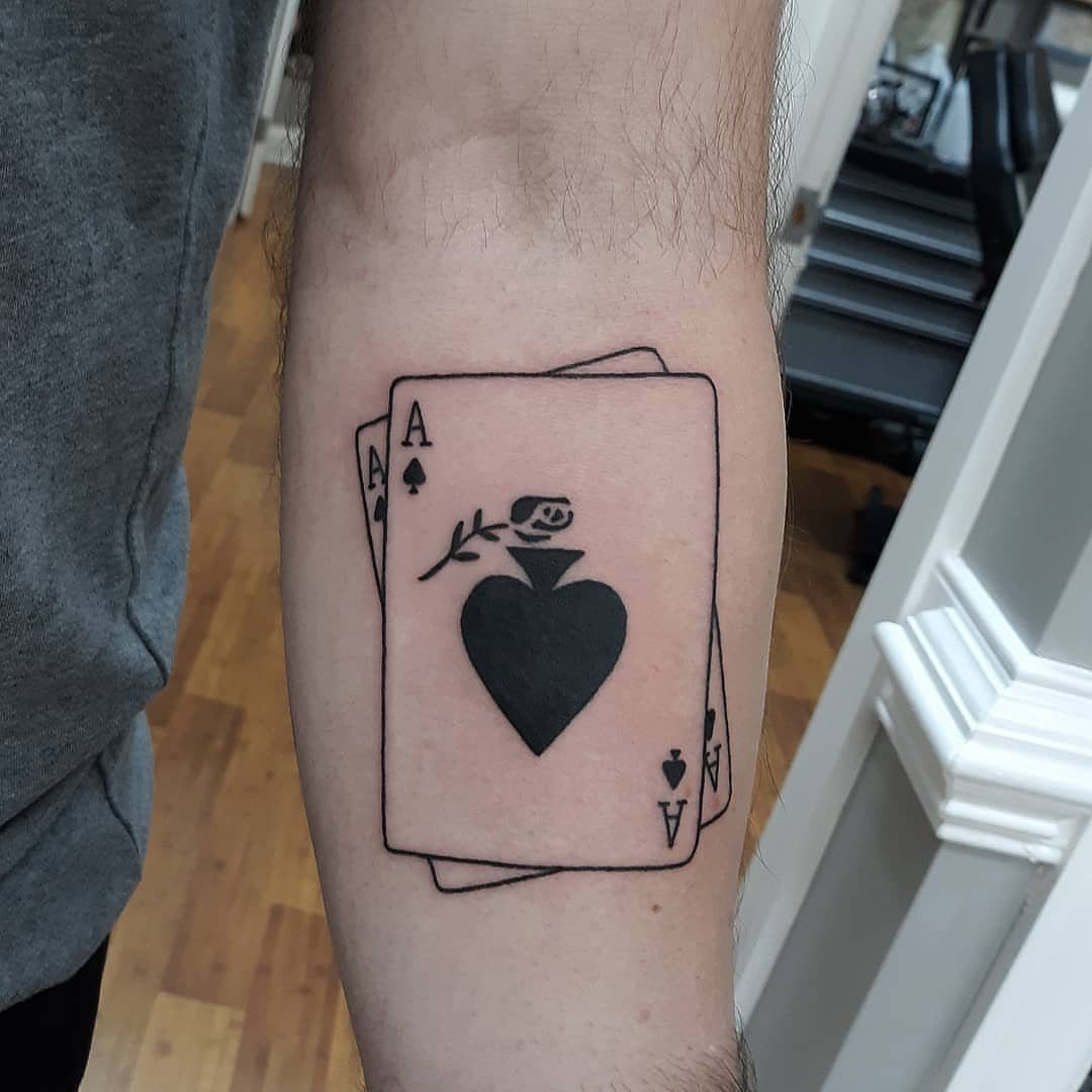 Ace of Spades playing card tattoo with a small rose on a forearm