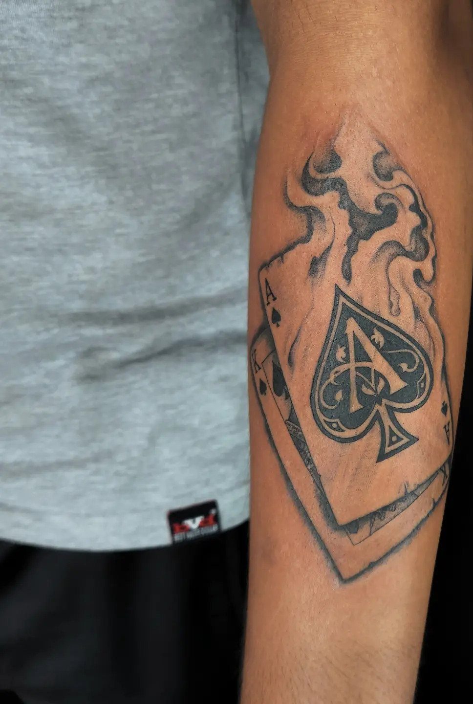Ace of Spades playing card tattoo with flames on a person's forearm