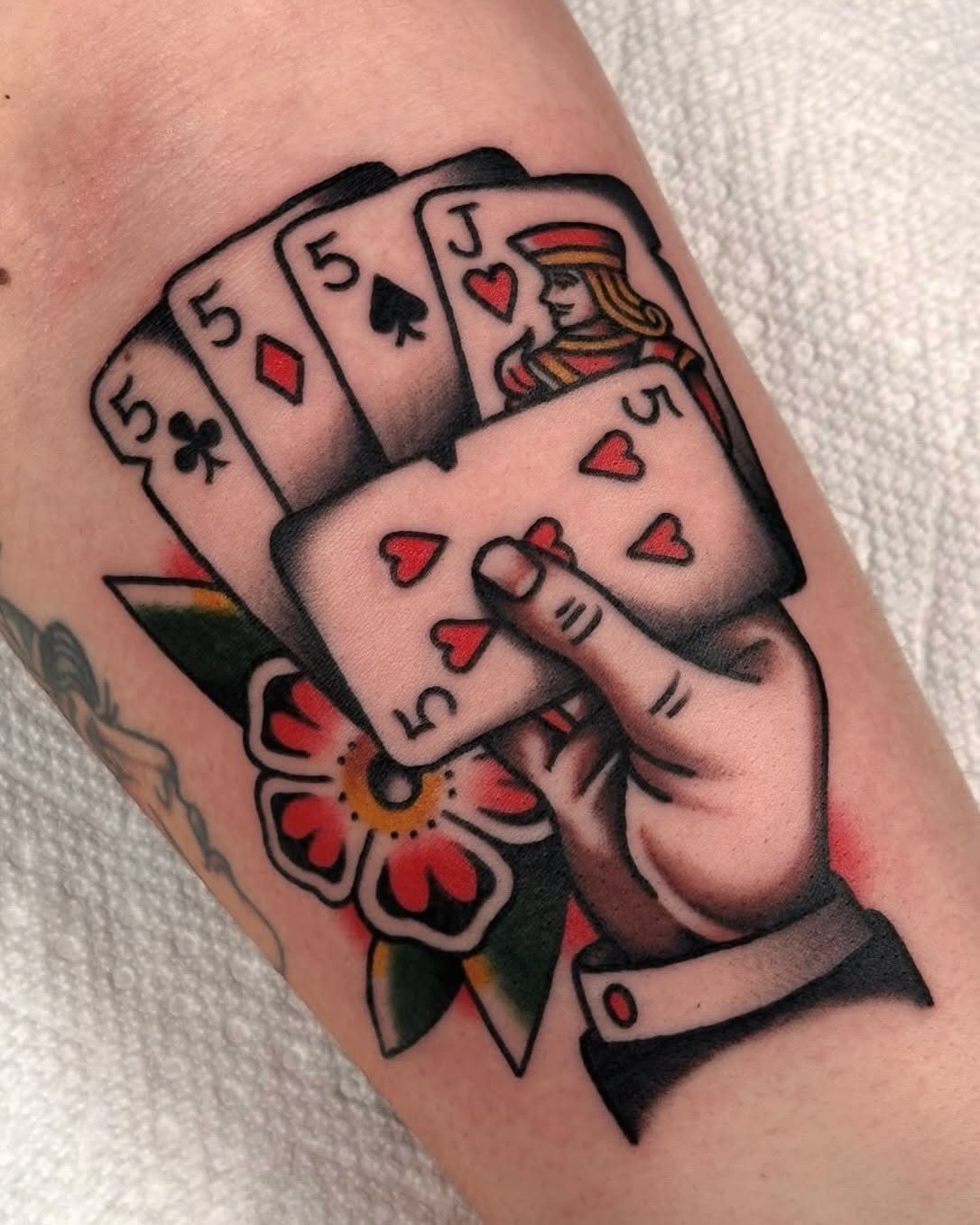 Hand holding playing cards tattoo with a red flower on a person's arm