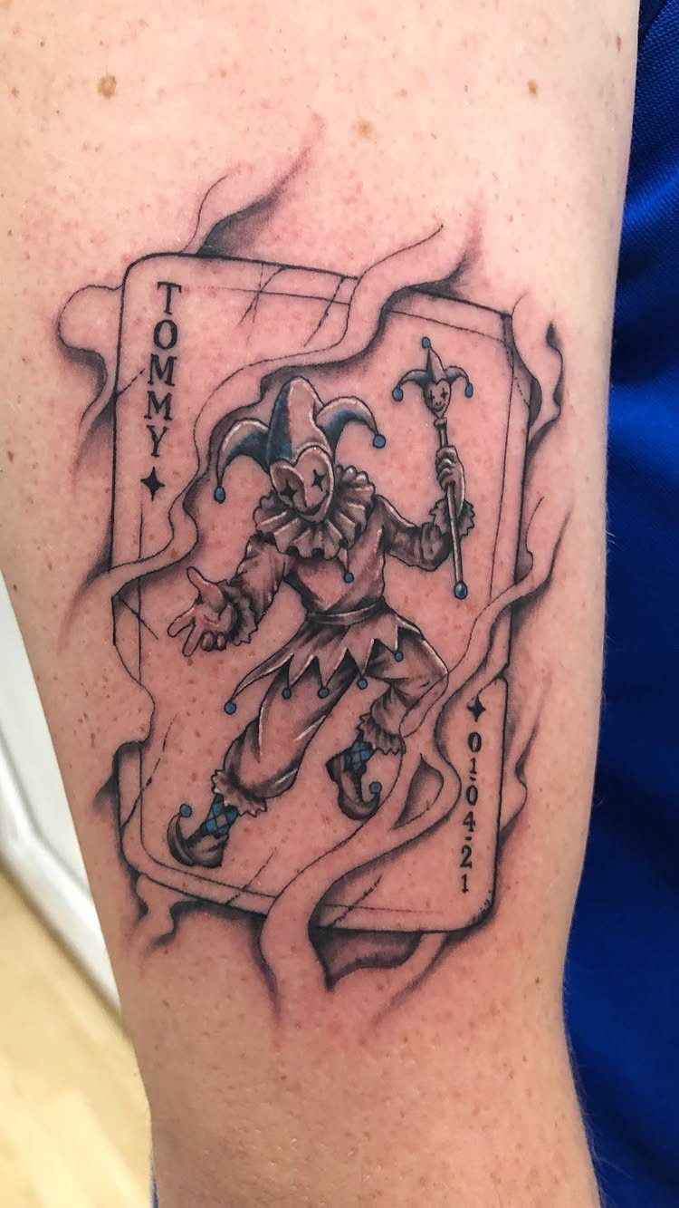 Joker playing card tattoo on an arm with smoke and jester figure