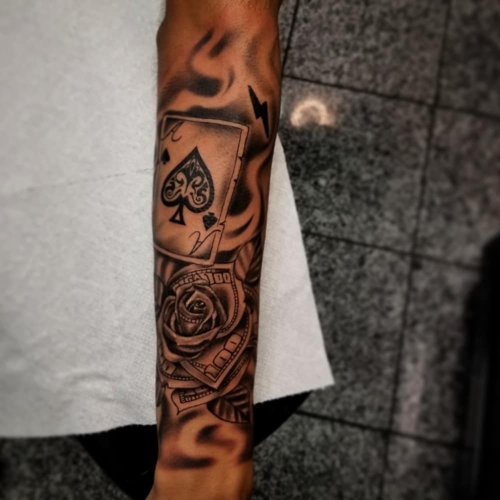 Forearm tattoo featuring an Ace of Spades, a rose, and hundred dollar bills.