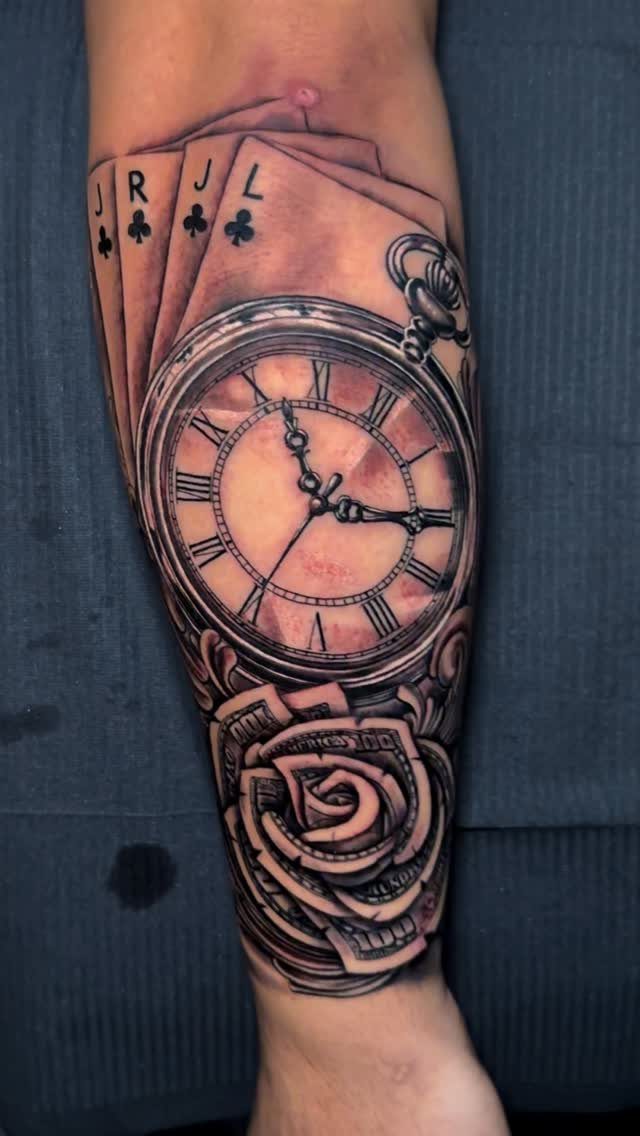 Forearm tattoo featuring a pocket watch, a rose, and playing cards in grey ink
