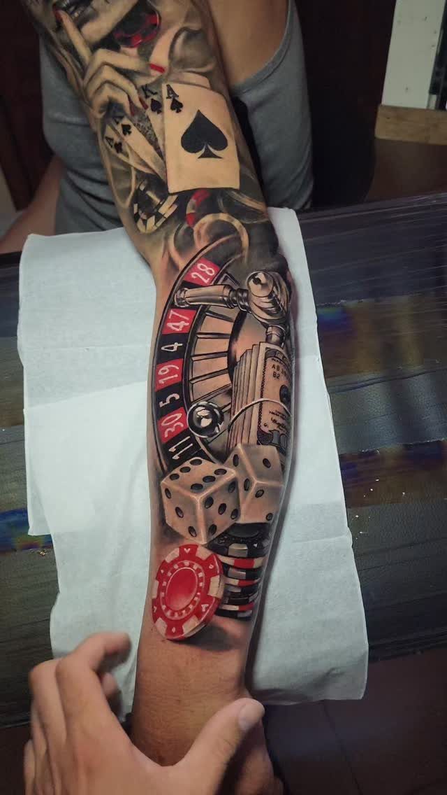 Tattoo sleeve on an arm featuring playing cards, roulette wheel, dice, and casino chip.